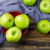 Green apples in a bowl on wooden and textile background, flat lay. GRANNY SMITH APPLE